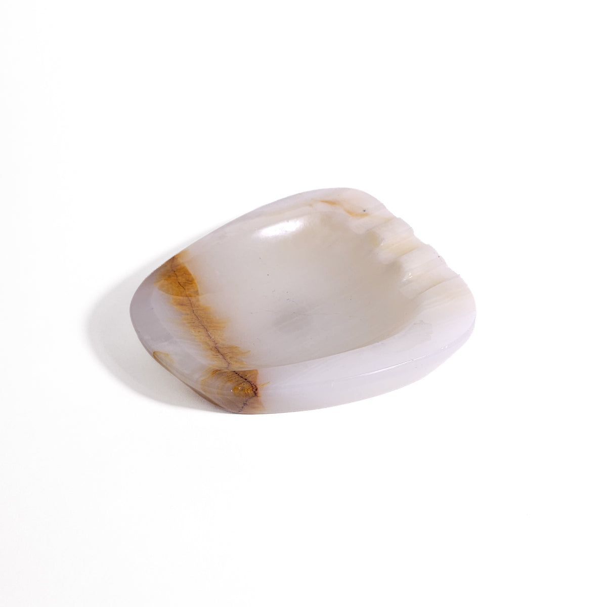 An organic, soft-cornered dish carved from translucent natural onyx featuring subtle creamy white banding, a warm caramel vein accent, and rest notches.