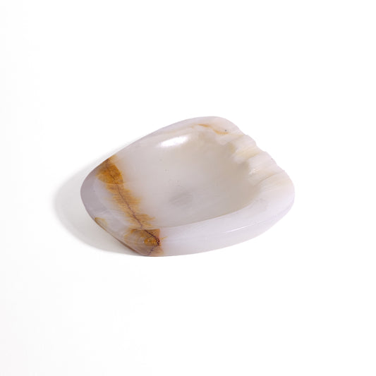 An organic, soft-cornered dish carved from translucent natural onyx featuring subtle creamy white banding, a warm caramel vein accent, and rest notches.